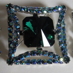 Puede incluir: Un conjunto de joyas de pedrer&iacute;a verde esmeralda y azul que incluye un broche con una piedra grande de color verde esmeralda rodeada de pedrer&iacute;a azul m&aacute;s peque&ntilde;a y un par de pendientes a juego.