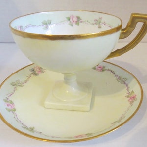 May include: A vintage teacup and saucer set with a delicate floral design. The cup has a gold rim and a footed base. The saucer has a matching floral design and a gold rim.