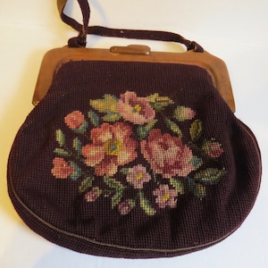 May include: A vintage brown purse with a wooden frame and a floral embroidered design. The embroidery features pink, green, and yellow flowers.