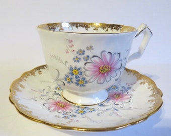 May include: A white teacup and saucer with a floral pattern in shades of pink, blue, and yellow. The cup and saucer have a gold trim.