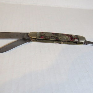 May include: A multi-blade pocket knife with a green and white handle with red accents. The knife has a small blade, a larger blade, and a small awl.