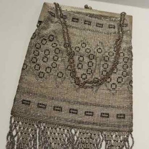 May include: A silver mesh purse with a chain strap and fringe detail. The purse has a geometric pattern and is made of metal.