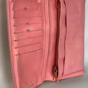 May include: Open, coral-colored leather wallet with multiple card slots and a zippered compartment. The wallet is open, revealing its interior. The brand name "CHANEL" is visible on the inside. The wallet is made of a soft, textured leather.