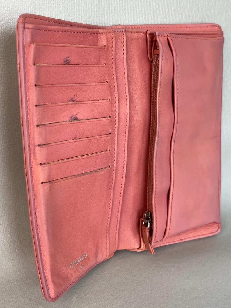 May include: Open, coral-colored leather wallet with multiple card slots and a zippered compartment. The wallet is open, revealing its interior. The brand name "CHANEL" is visible on the inside. The wallet is made of a soft, textured leather.