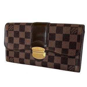 May include: A rectangular wallet featuring a brown and dark brown checkered pattern with the text Louis Vuitton Paris printed on the surface. The wallet includes a central dark brown leather strap and a gold-toned metal clasp closure.