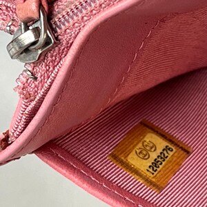 May include: Close-up of a pink leather wallet, partially open, revealing a light pink interior lining. A silver zipper and a small, rectangular label with the number "12053276" are visible. The wallet appears to be made of high-quality materials.