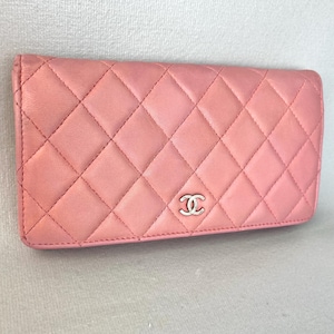 May include: A pink quilted leather wallet with a silver-tone logo. The wallet has a diamond pattern and a rectangular shape. The stitching is visible, and the wallet appears to be made of high-quality materials.