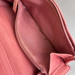 May include: Open pink leather wallet with a silver zipper and a pink fabric interior. The wallet is open, revealing the inside compartments and a coin pouch. The leather appears to be smooth and the wallet is empty.