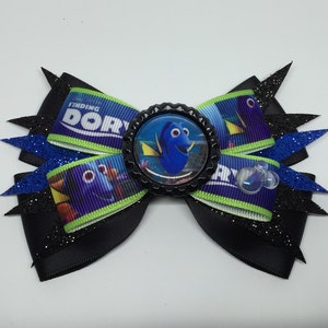 Peut inclure: Un nœud pour cheveux fait à la main avec le film Le Monde de Dory. Le nœud a une base noire avec des accents de paillettes bleues et noires. Le centre présente une image du personnage Dory dans un bouchon de bouteille noir. Un accessoire amusant.