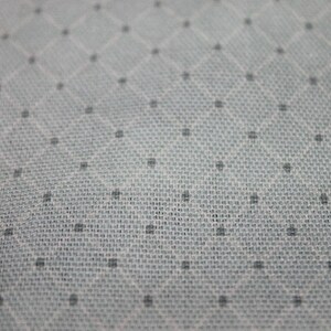 May include: Close-up of a white fabric with a subtle diamond pattern and small black dots.