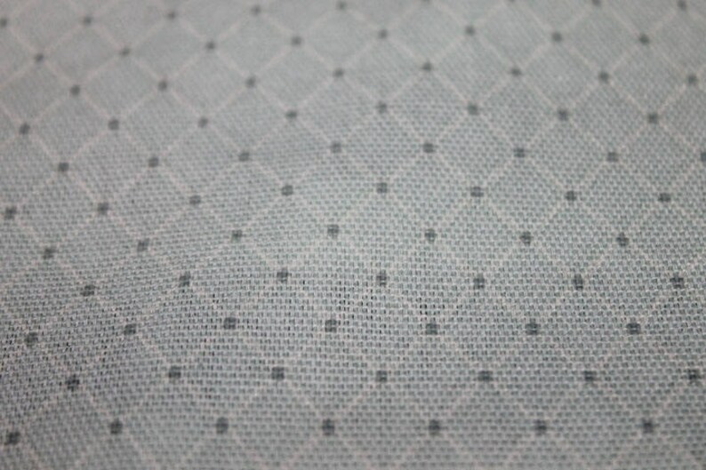 May include: Close-up of a white fabric with a subtle diamond pattern and small black dots.