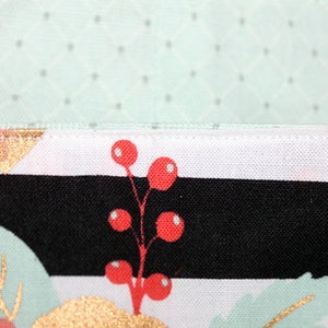 May include: Close-up of a seam on a fabric with a black and white striped pattern, a gold triangle, and red berries on a white background.