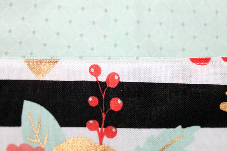 May include: Close-up of a seam on a fabric with a black and white striped pattern, a gold triangle, and red berries on a white background.