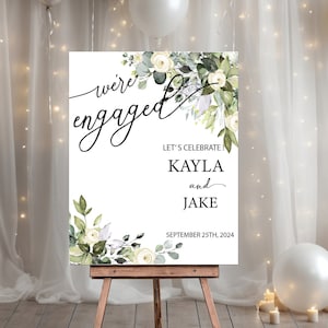 May include: White and green floral engagement announcement sign with the text "we're engaged" and "Let's celebrate! Kayla and Jake September 25th, 2024".