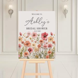 May include: Welcome to Ashley's Bridal Shower sign with a floral design featuring pink and orange flowers on a white background. The date of the shower is 03.27.2025.