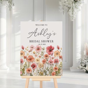 May include: A white welcome sign with a floral border and the text "Welcome to Ashley's Bridal Shower 03.27.2025".