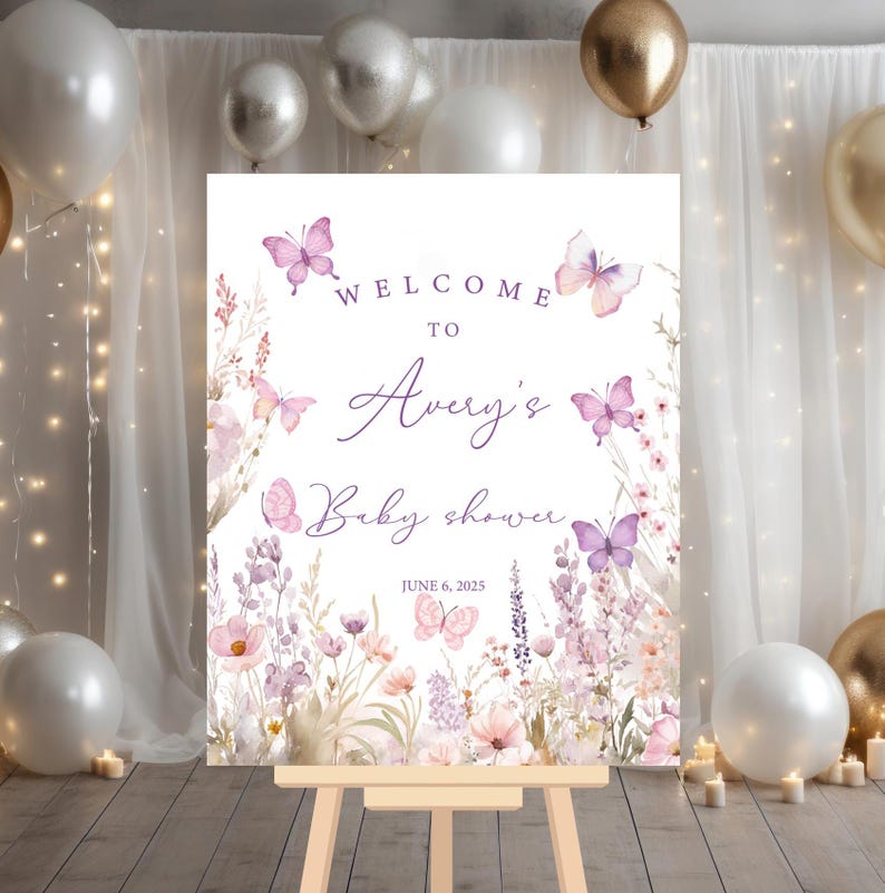 May include: Welcome to Avery's Baby Shower sign with a purple and white floral design featuring butterflies. The sign is on a wooden easel and has the date June 6, 2025.