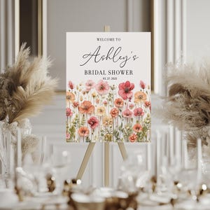 May include: Welcome to Ashley's Bridal Shower sign with a floral design featuring pink, orange, and yellow flowers on a white background. The date of the shower is March 27, 2023.