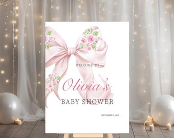 May include: A baby shower sign on an easel. The sign features a large pink bow with floral accents and the text "Welcome to Olivia's Baby Shower" in pink script. The date "September 7, 2025" is also displayed.