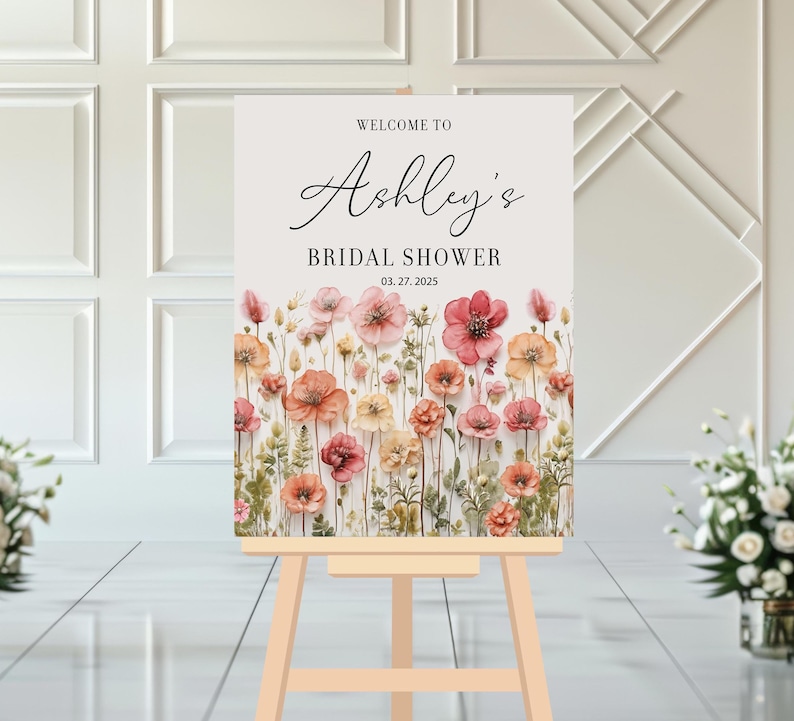 May include: Welcome to Ashley's Bridal Shower sign with a watercolor floral design featuring pink, peach, and yellow flowers on a white background.