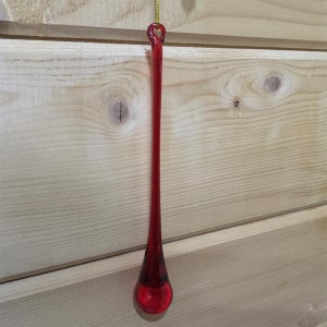 Könnte beinhalten: Ein langer, roter gläserner Tropfen-Anhänger mit einer goldenen Schnur zum Aufhängen.