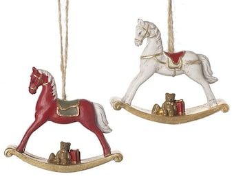 May include: Two rocking horse ornaments, one red and one white, with a teddy bear and a gift box on each rocking base. Both ornaments have a gold trim and a twine hanger.