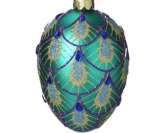 May include: A teal blue glass Christmas ornament with a gold and purple peacock feather design. The ornament has blue glitter accents and is decorated with blue jewel-like accents.