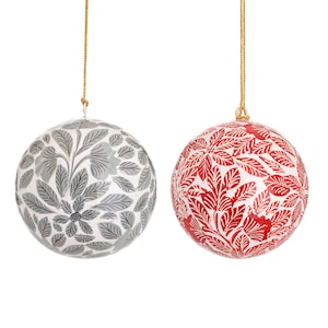 Pode incluir: Dois enfeites de Natal com padrões florais. Um enfeite é branco com desenhos florais cinzentos, e o outro é branco com desenhos florais vermelhos.