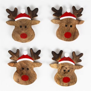 Pu&ograve; includere: Quattro sottobicchieri di legno a forma di renna con nasi rossi e cappelli di Babbo Natale bianchi. Le renne sono dipinte su uno sfondo di legno marrone.