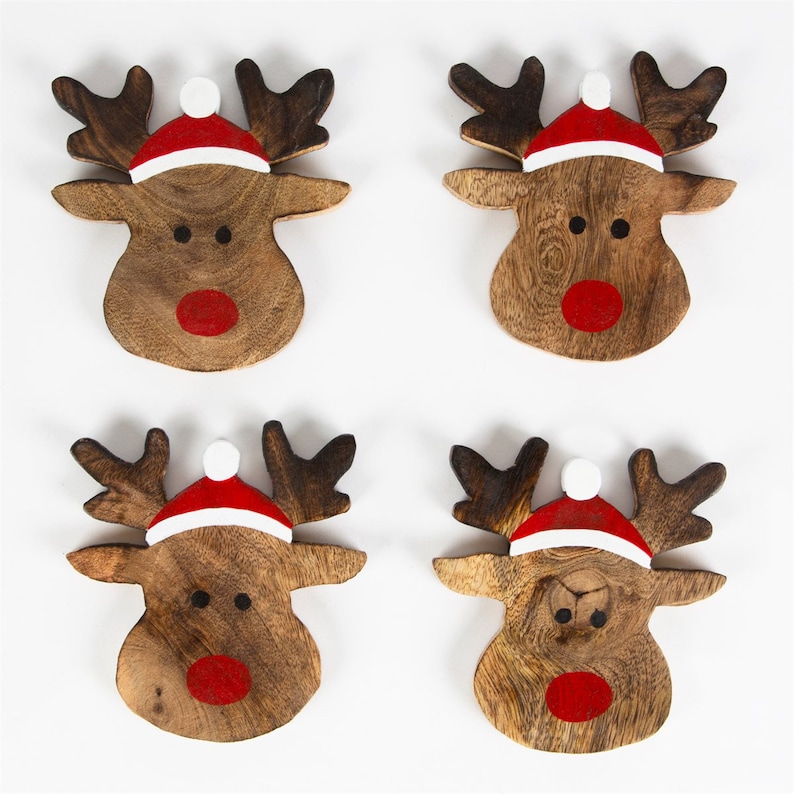 Pu&ograve; includere: Quattro sottobicchieri di legno a forma di renna con nasi rossi e cappelli di Babbo Natale bianchi. Le renne sono dipinte su uno sfondo di legno marrone.