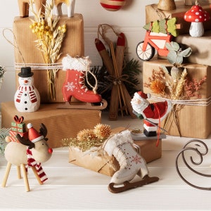May include: Assortment of wooden Christmas ornaments, including a snowman, reindeer, Santa Claus, ice skates, and a Christmas tree. The ornaments are decorated with red, white, and blue paint and have a rustic, handmade look.