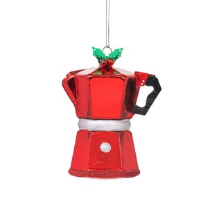 May include: A red Christmas tree ornament in the shape of a coffee pot. The ornament has a silver band, a black handle, and is decorated with green holly and red berries. A silver string is attached for hanging.