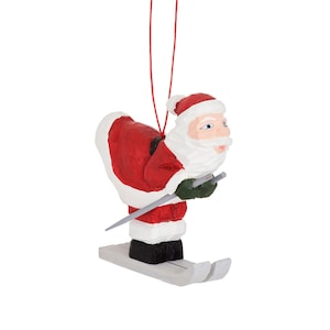 May include: A wooden Christmas ornament of Santa Claus skiing down a snowy slope. He is wearing a red suit with white trim and a white beard. He is holding ski poles in his hands.