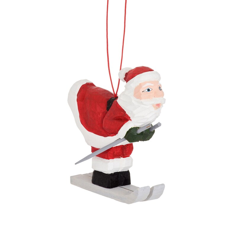 May include: A wooden Christmas ornament of Santa Claus skiing down a snowy slope. He is wearing a red suit with white trim and a white beard. He is holding ski poles in his hands.