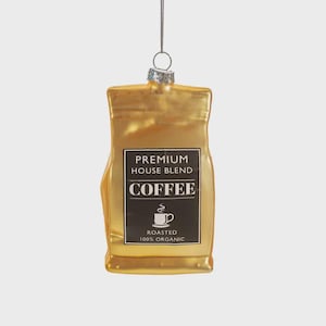 May include: A gold-colored coffee bag ornament with a silver cap and hanging loop. The black label reads "PREMIUM HOUSE BLEND COFFEE" with a coffee cup graphic and "ROASTED 100% ORGANIC". A festive decoration for coffee lovers.