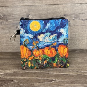 May include: A small, square zippered pouch featuring a painting of pumpkins under a starry night sky. The artwork is in the style of Van Gogh, with vibrant blues, yellows, and oranges. A silver-colored clasp is attached to the side.