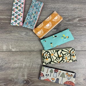 May include: Six different fabric pencil cases with zipper closures. The cases feature various patterns including floral, geometric, and mushroom designs.