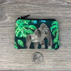 Puede incluir: Una peque&ntilde;a bolsa con cremallera verde y negra con un gorila y hojas tropicales impresas.
