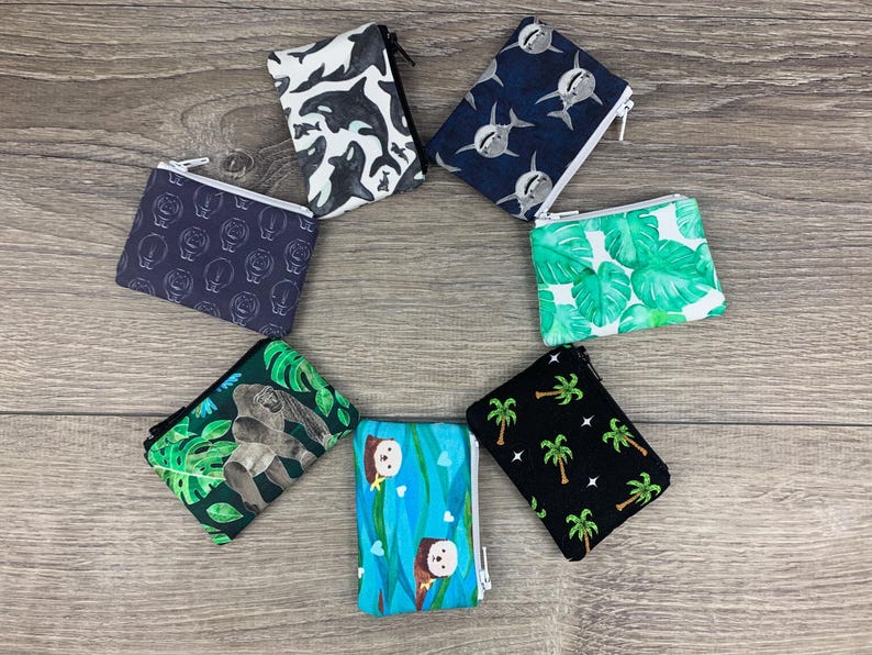 Puede incluir: Siete bolsas con cremallera diferentes con varios dise&ntilde;os. Las bolsas est&aacute;n hechas de tela y tienen una variedad de patrones, que incluyen animales, plantas y formas geom&eacute;tricas. Las bolsas est&aacute;n todas cerradas y dispuestas en c&iacute;rculo sobre una superficie de madera.