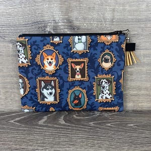 May include: A navy blue zippered pouch featuring framed portraits of various dog breeds. The pouch has a black zipper and a small tassel. The background is a dark blue with a scrolling pattern.
