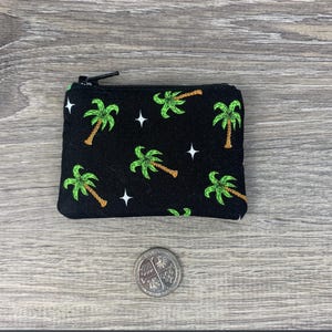 Puede incluir: Una bolsa negra con cremallera con estampado de palmeras. La bolsa tiene estrellas blancas y palmeras verdes sobre un fondo negro.