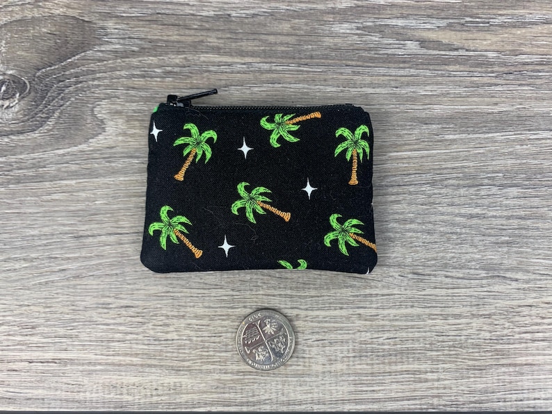 Puede incluir: Una bolsa negra con cremallera con estampado de palmeras. La bolsa tiene estrellas blancas y palmeras verdes sobre un fondo negro.