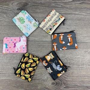 May include: Six small zippered pouches with different colorful patterns. The pouches feature designs of unicorns, foxes, musical notes, tacos, cats, and hedgehogs.