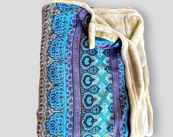 May include: A blue and purple patterned throw blanket with a soft, beige fleece lining. The blanket is folded in half and the fleece lining is visible.