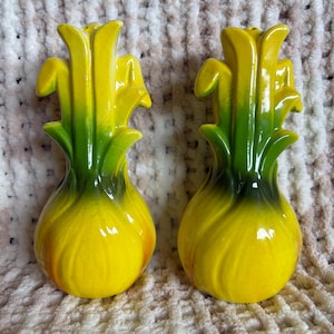 May include: A pair of ceramic salt and pepper shakers shaped like stylised yellow and green daffodils. Each shaker features a rounded base that tapers upwards into a flared, petal-like top, with a smooth, glossy finish and vibrant colour gradients.