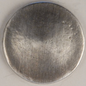 May include: A silver coin with a smooth, slightly textured surface. The coin has a circular shape and a slightly raised edge.