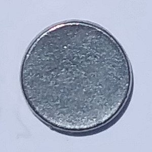 May include: A silver-colored round magnet with a textured surface.