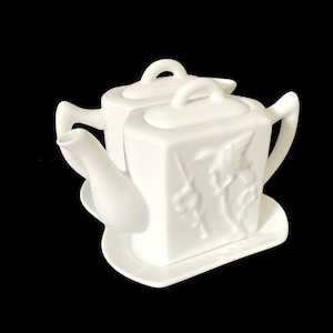 May include: A white porcelain teapot set with a square body and a matching lid. The teapot features a raised relief design and sits on a matching saucer. The set is all white and has a classic, elegant design.