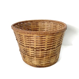 May include: A round, woven basket made of natural brown and tan bamboo. The basket has a wide, open top and a slightly flared base.