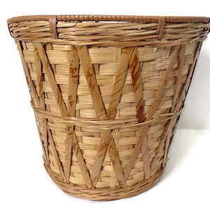 May include: A woven bamboo basket with a rounded bottom and a flared top. The basket is constructed with a crisscross pattern and reinforced with horizontal bands. The natural bamboo color is accented with darker brown streaks.